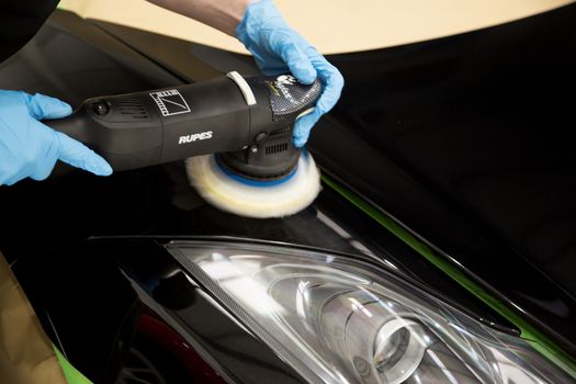 Detailer using a rotary machine on a sports car panel