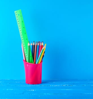 pink stationery glass with multi-colored wooden pencils and , blue background, copy space