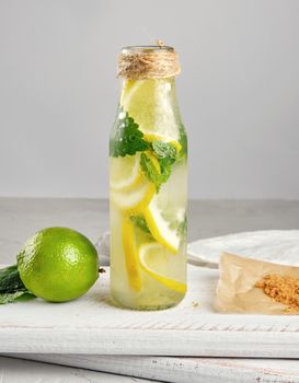 summer refreshing drink lemonade with lemons, mint leaves, lime in a glass bottle, next to the ingredients for making a cocktail