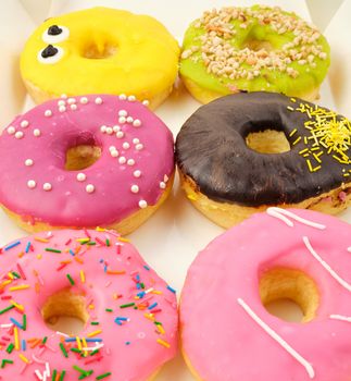 six round various sweet donuts with sprinkles in a paper white box, top view, selective focus 