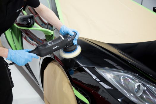 Detailer using a rotary machine on a sports car panel