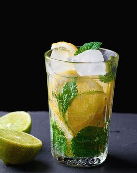 cold drink made from pieces of lemon, lime and leaves of green mint in a glass with water drops, next to ingredients for making lemonade