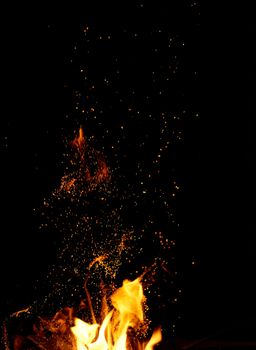 large burning bonfire with flame and orange sparks that fly in different directions on a black background