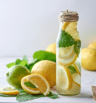 refreshing drink lemonade with lemons, mint leaves, lime in a glass bottle, next to the ingredients for making a cocktail