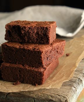 stack of baked square pieces of chocolate brownie cake on brown parchment paper, top view