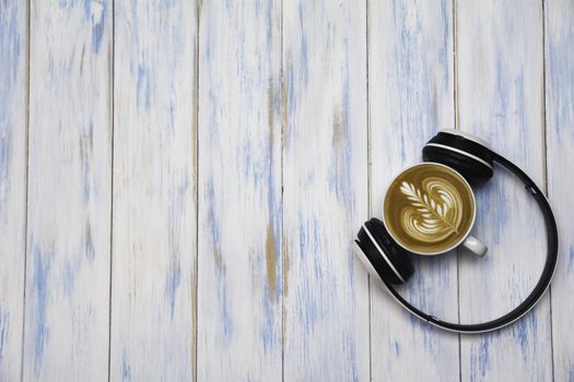 A cup of coffee with headphone on wooden table. Top view of coffee latte art with copy space. Drink and art concept.