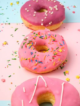 three round different sweet donuts with sprinkles on a pink background, top view, close up