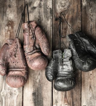 two pairs of leather vintage boxing gloves hanging on a nail, old wooden planks background, concept of the end of a sporting career