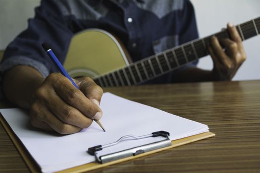 Composer holding pencil and writing lyrics in paper. Musician playing acoustic guitar.