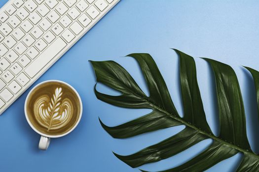 A cup of coffee with keyboard and copy space on blue background. Office desk and drink concept.