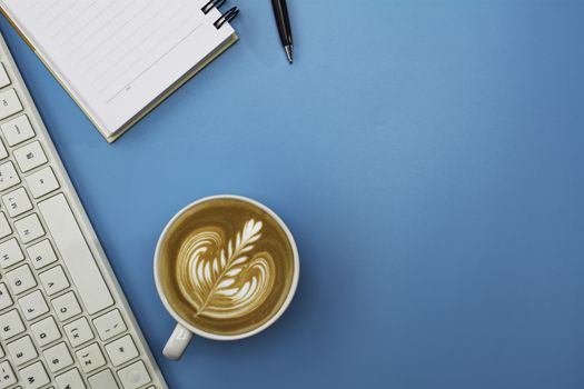 A cup of coffee with keyboard and copy space on blue background. Office desk and drink concept.