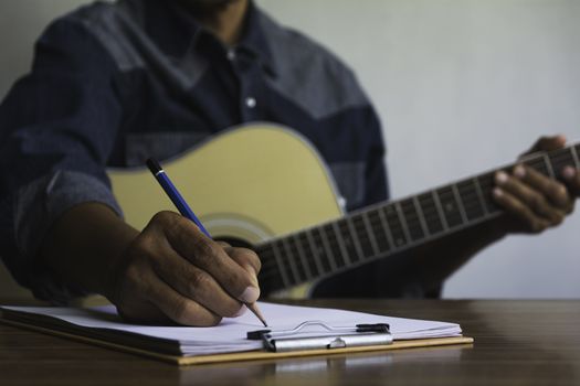 Composer holding pencil and writing lyrics in paper. Musician playing acoustic guitar.