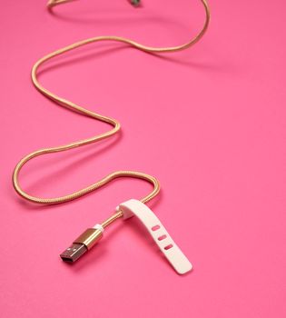 golden usb cable for charging with electricity equipment in textile winding on a pink background