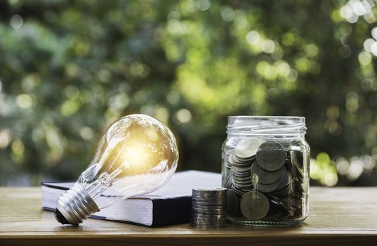 Energy saving light bulb with coins in glass jar for saving, financial and accounting concept and copy space for insert text.