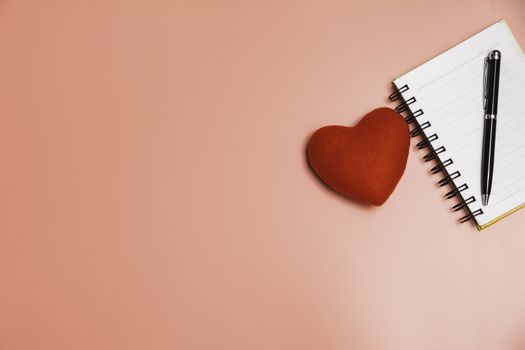 Top view of open book red heart. Book open with pen on pink background.