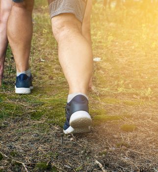 adult man in black shorts runs in the coniferous forest against the bright sun, concept of a healthy lifestyle and running in the fresh air, back view