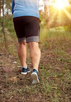 adult man in blue clothes and black shorts runs along the coniferous forest against the bright sun,  concept of a healthy lifestyle and running in the fresh air