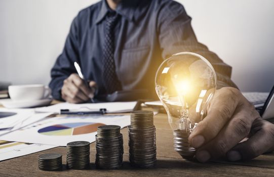Business man holding a light bulb with coins money and copy space for accounting, ideas and creative concept.