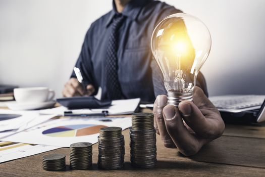 Business man holding a light bulb with coins money and copy space for accounting, ideas and creative concept.