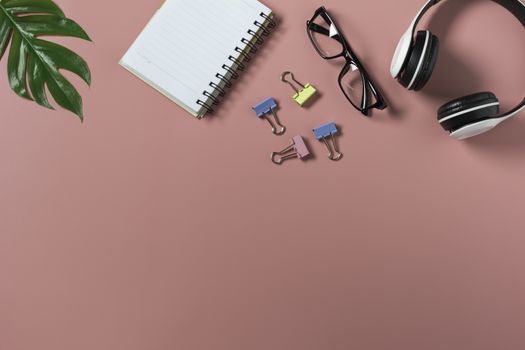 Top view with the glasses, note book and headphone on pink backgroup. Cluttered office desk background.