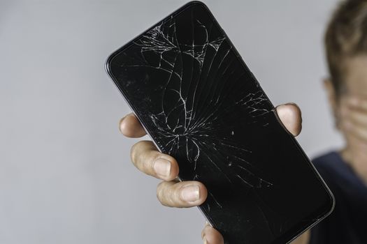 Woman holding a broken touch screen of smart phone on grey background.