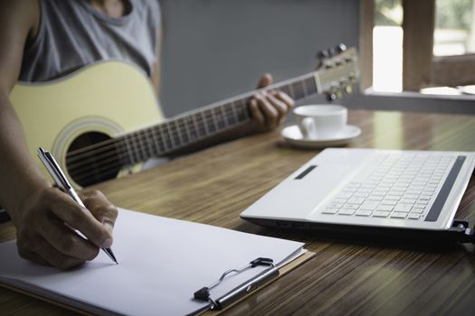 Composer holding pencil and writing lyrics in paper. Musician playing acoustic guitar.