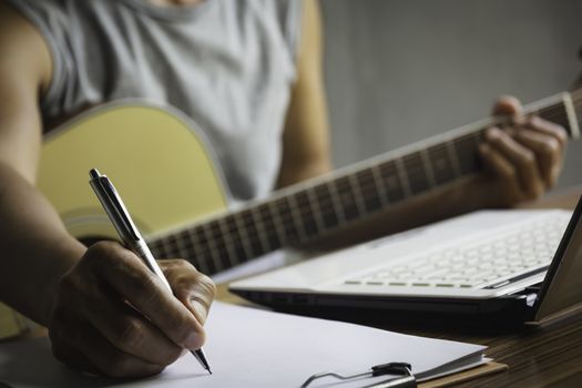 Composer holding pencil and writing lyrics in paper. Musician playing acoustic guitar.