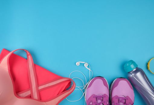pink women's sneakers, bottle of water, clothes and bras for sports on a  blue background, top view, copy space