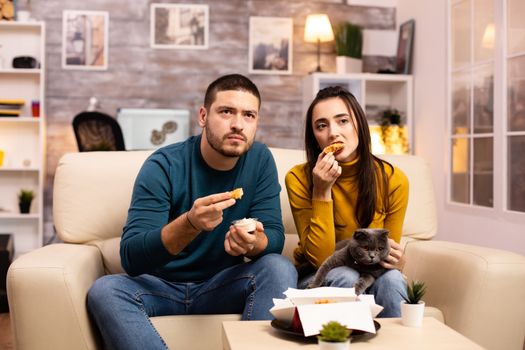 Young couple eating fried chicken in front of the TV in the living room