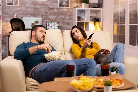 Beautiful young couple watching TV and eating fast food takeaway in the living room