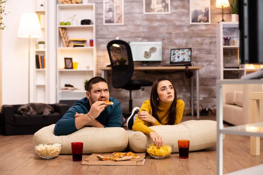 Couple sitting on the floor and watching TV in their living room.