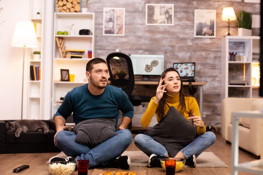 Couple sitting on the floor and watching TV in their living room.