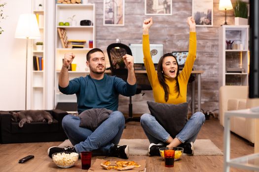 Couple sitting on the floor and watching TV in their living room.