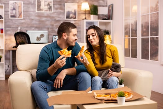 Gorgeous young couple eating pizza while watching TV in the living room sitting on the sofa