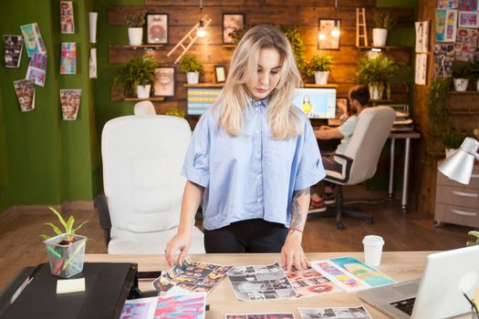 Caucasian female designer checking her interns designs. Man working on laptop in the background.