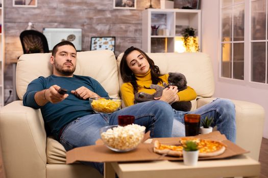 Beautiful young couple watching TV and eating fast food takeaway in the living room