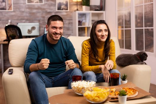 Happy couple cheering for their favourite team while watching TV in he living room.