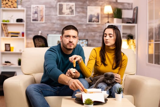 Young couple eating fried chicken in front of the TV in the living room