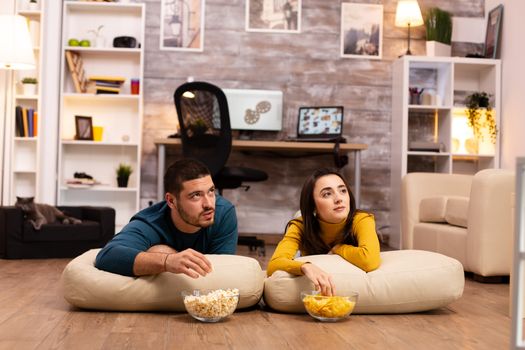 Couple sitting on the floor and watching TV in their living room.