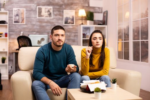 Young couple eating fried chicken in front of the TV in the living room