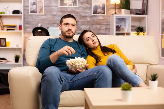 Handsome couple at home eating pop corn and watching TV on the sofa in the living room