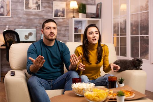 Couple cheering for their favourite team while watching TV and eating fast food