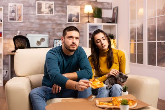 Gorgeous young couple eating pizza while watching TV in the living room sitting on the sofa