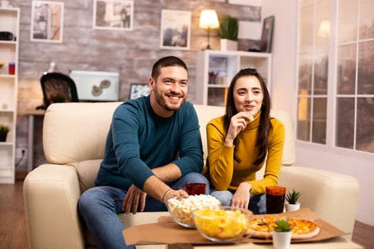 Beautiful young couple watching TV and eating fast food takeaway in the living room