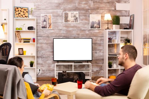 Couple looking at isolated TV screen in cozy living room while eating takeaway food