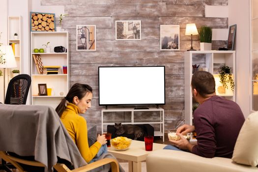 Couple looking at isolated TV screen in cozy living room while eating takeaway food