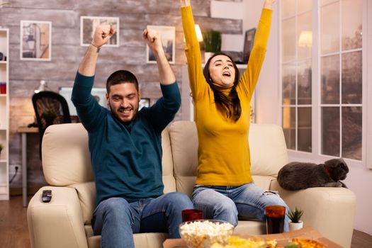 Happy couple cheering for their favourite team while watching TV in he living room.