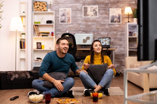 Couple sitting on the floor and watching TV in their living room.