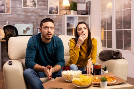 Couple cheering for their favourite team while watching TV and eating fast food