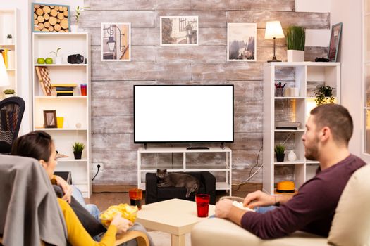 Couple looking at isolated TV screen in cozy living room while eating takeaway food